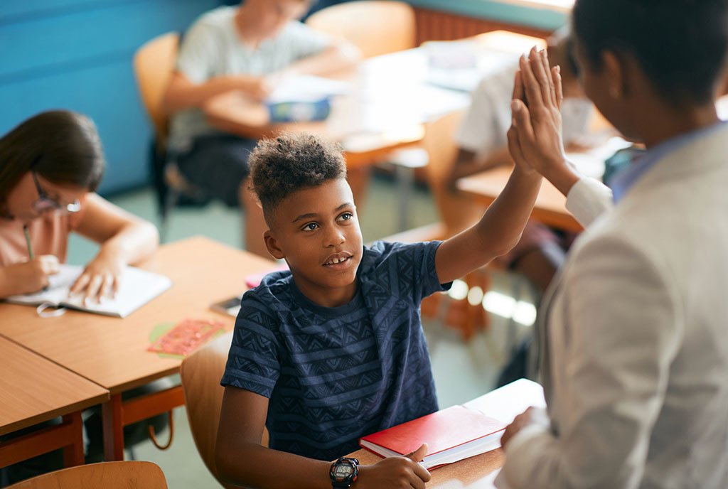 A Black boy student high fives his Black teacher in an elementary school classroom