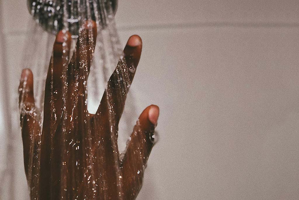 A Black man’s hand, reaching upwards under a steady shower stream.