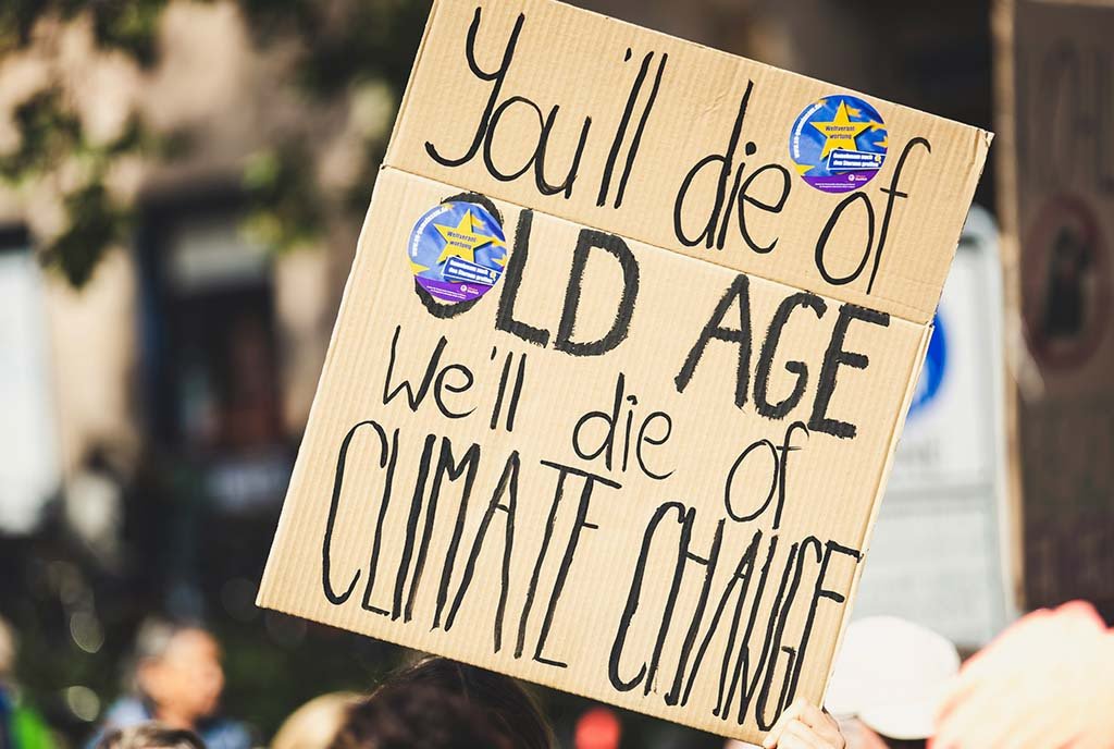 A cardboard protest sign that reads, “You’ll die of old age. We’ll die of Climate Change.”