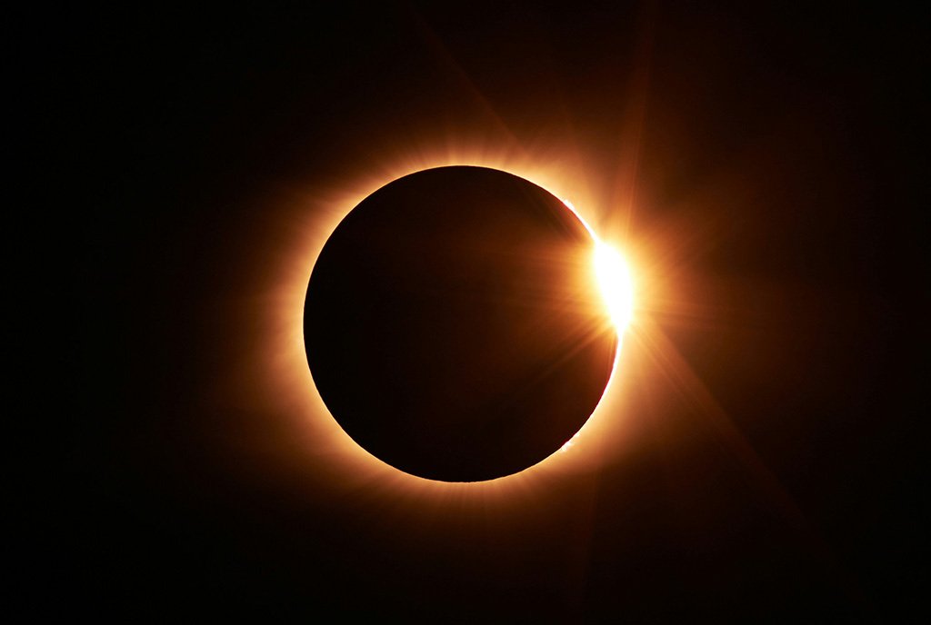 A total solar eclipse, with the moon covering most of the sun except for a small glare on the right side.