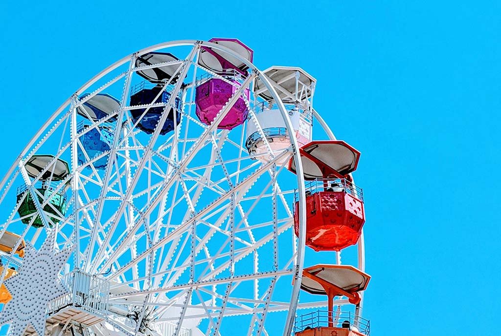 A revolving ferris wheel with colorful cars, against a blue sky.