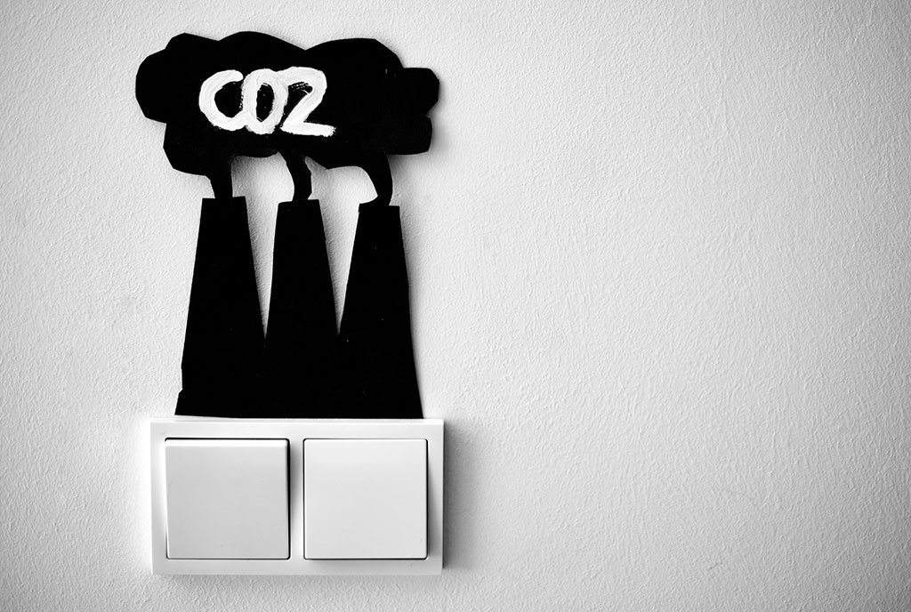 A light switch topped with a cardboard cutout of black smoke stacks emitting CO2.