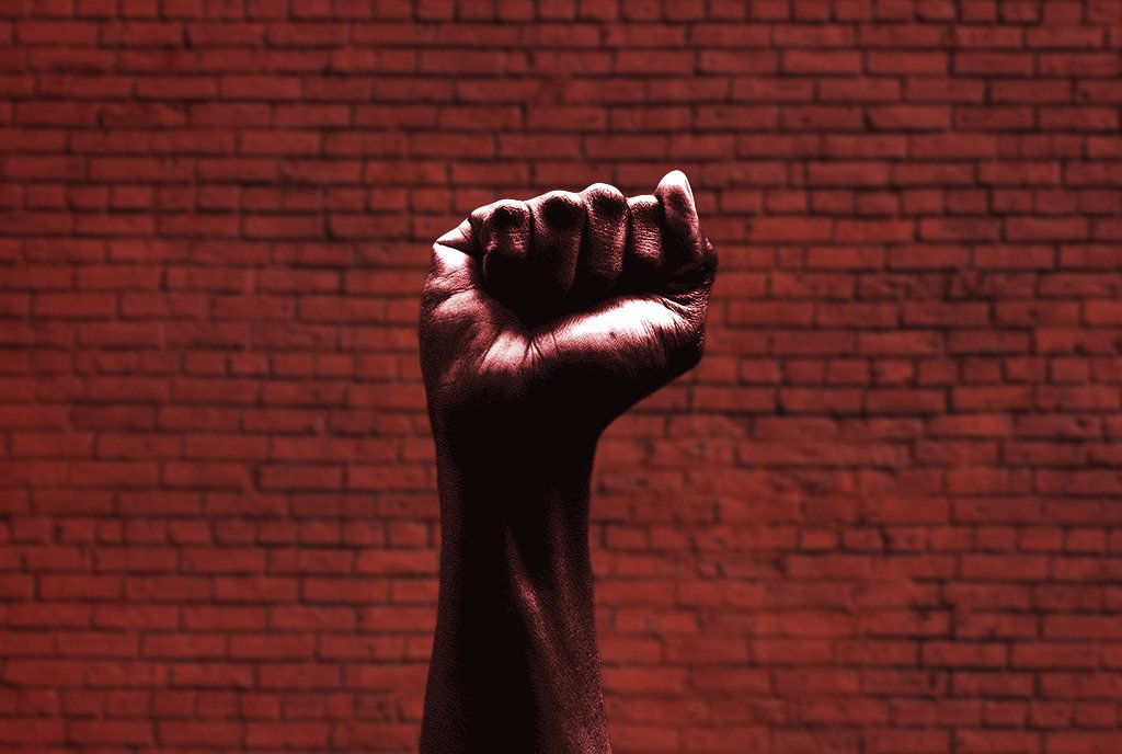 A fist is raised in front of a red brick wall.