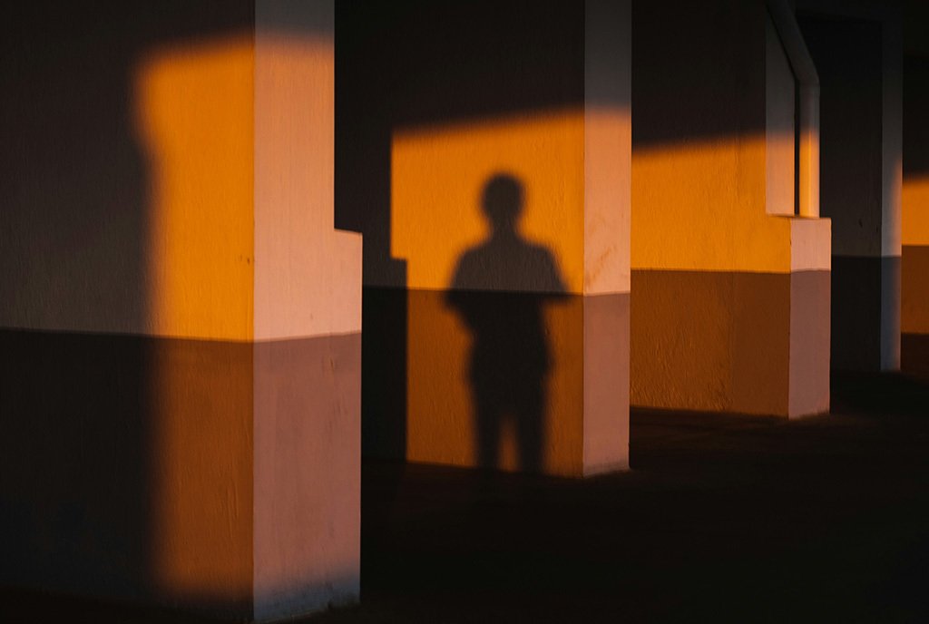 A shadow of a man casts onto a singular wall of several parallel hallway paths.