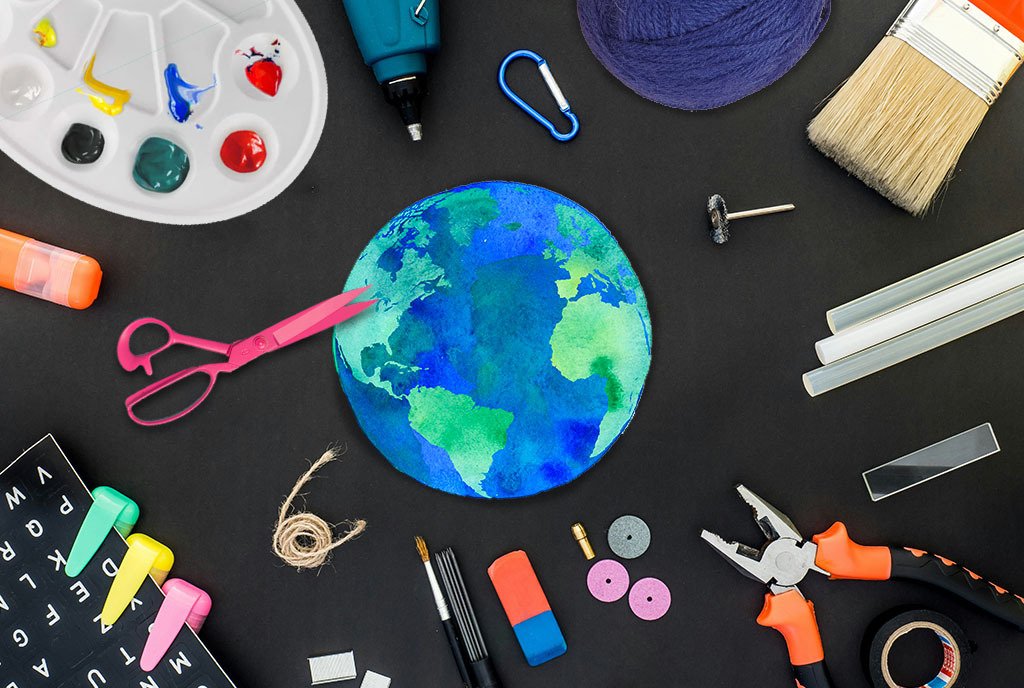 A small, crafted paper earth in surrounded by crafting supplies, like scissors, glue, twine, painting supplies, yarn, and writing utensils.