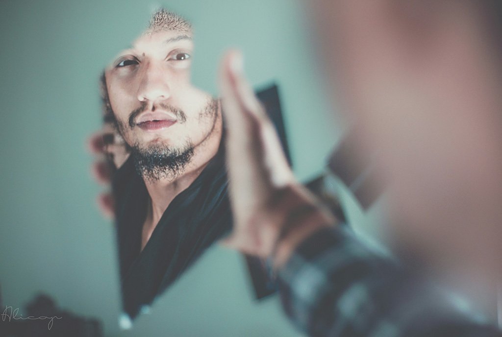 A North African man looks into a broken mirror with a serious expression on his face.