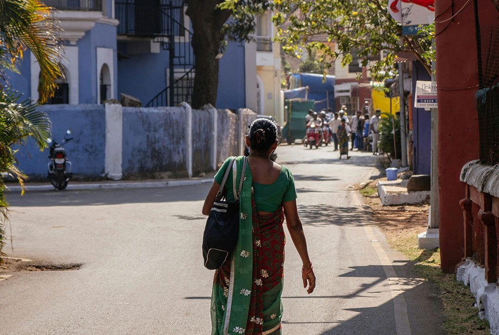 The back of an Indian woman wearing a red and green sari, as she walks home in extreme heat in Altinho, Panaji, Goa, India.
