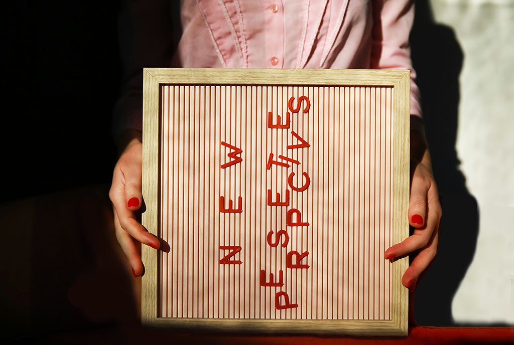 A person with red nails holding a letterboard sign on it’s side that reads, “New Perscpectives”