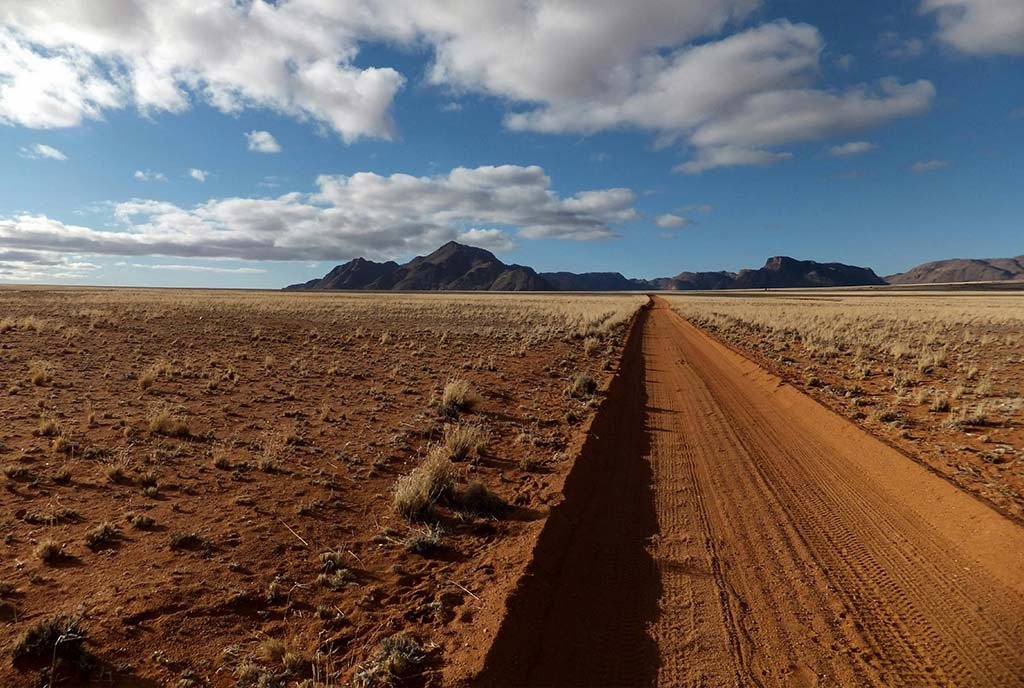 A wide shot of acres of desert land made of clay-colored sand with mountains in the background.