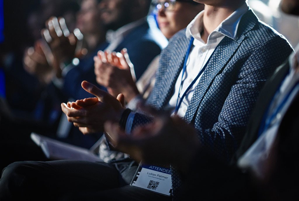 Close Up on Hands of a crowd of people clapping in dark Conference Hall during a political convention.