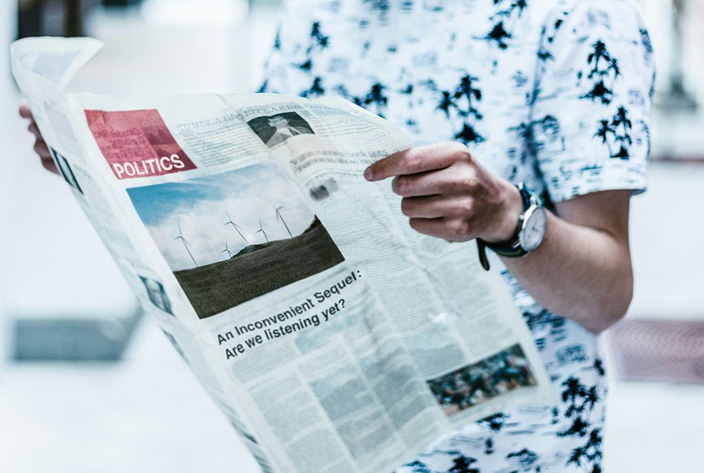 A man’s hands hold newspaper as he stands and reads it.