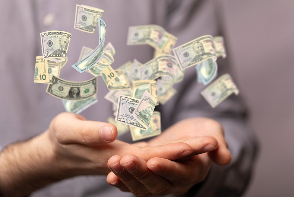 A person's hands cradling and releasing a flurry of money into the air.