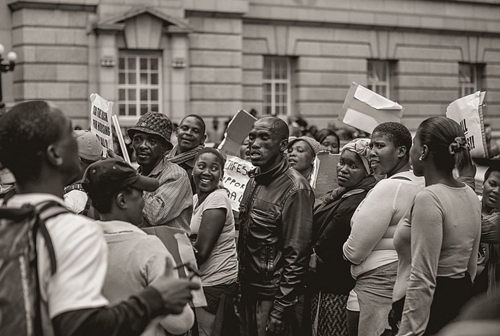 Unemployed and poor citizens protest in front of the Cape Town High Court with signs declaring that the wealthy should be taxed in order to generate funds to create affordable housing for the poor.