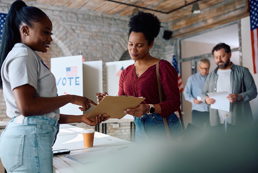 A Black woman polling place volunteer assisting another black woman to sign up for voting during USA elections