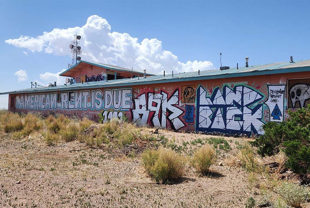 A photograph of skillful graffitti on the side of a building that reads, “American Rent is Due. Land Back”. Arizona, USA.