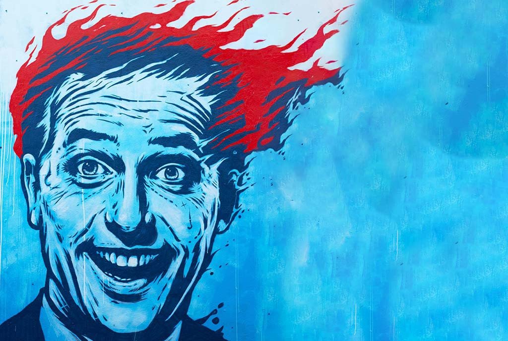 A graffitti painting of a man whose head is on fire, with smoke billowing from his scalp. Despite his fiery hair, he has a deranged smile on his face.