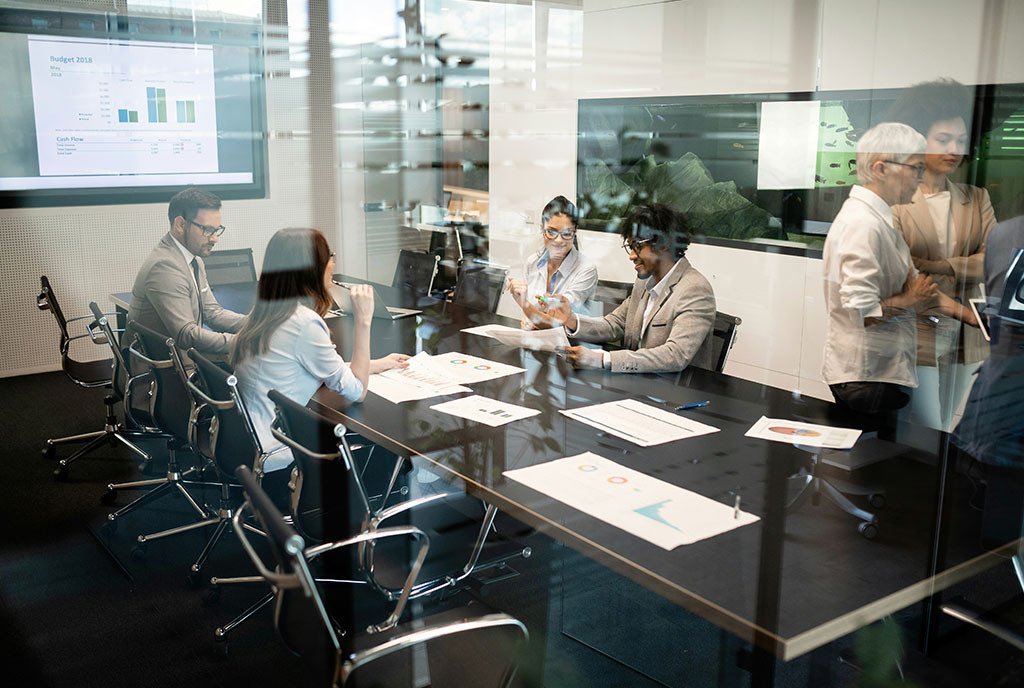 A group of diverse professionals work together in a conference room to assess budgeting documents.