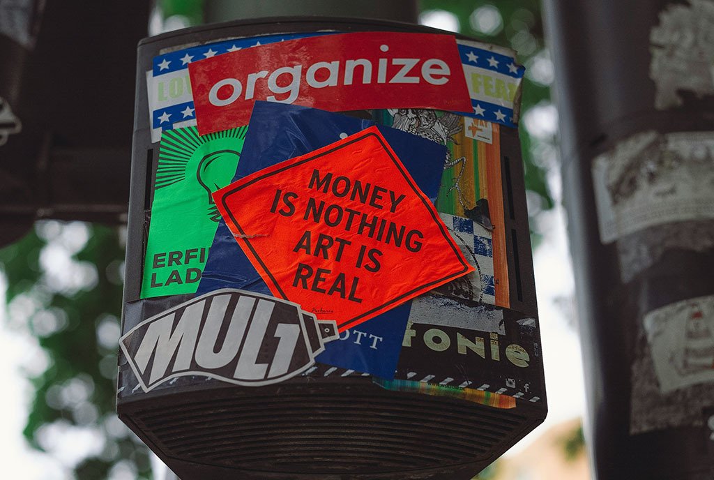  A red sticker affixed to a light post that reads, “Money is nothing. Art is Real.”