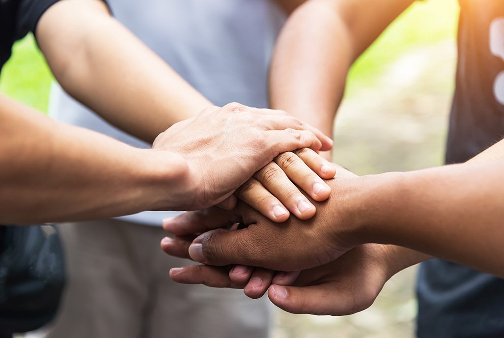 A group of people standing in a circle and stacking thier hands on top of each other in solidarity.