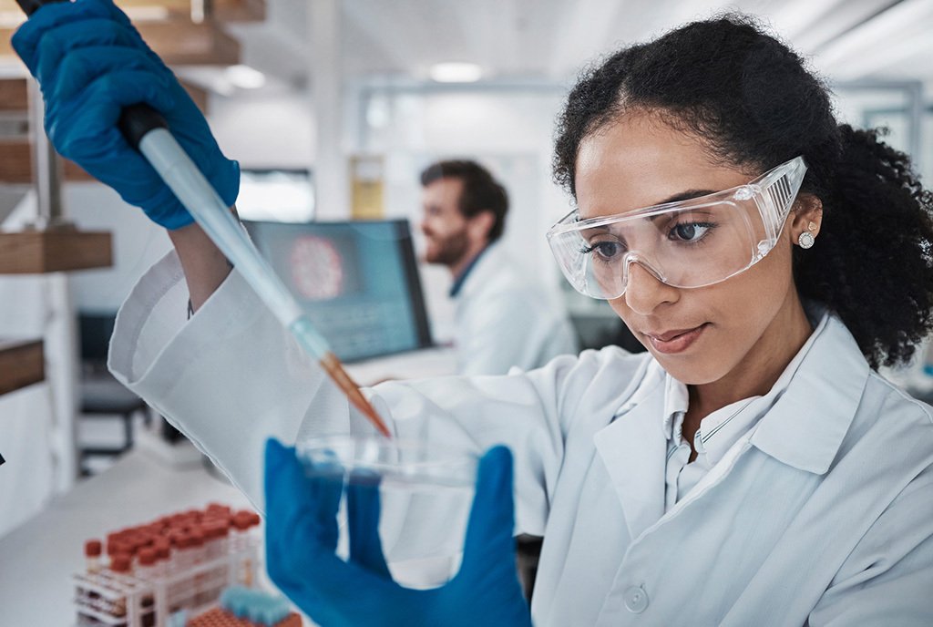 A Black woman scientist, in a research laboratory using a pipette to drop a liquid into petri dish in laboratory research.