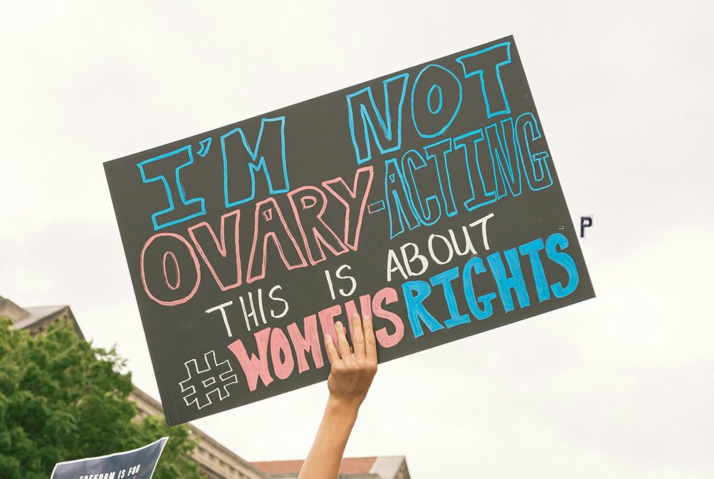 A woman holds up a sign at a protest that reads, “I’m not Ovary-Acting. This is about #WomensRights”