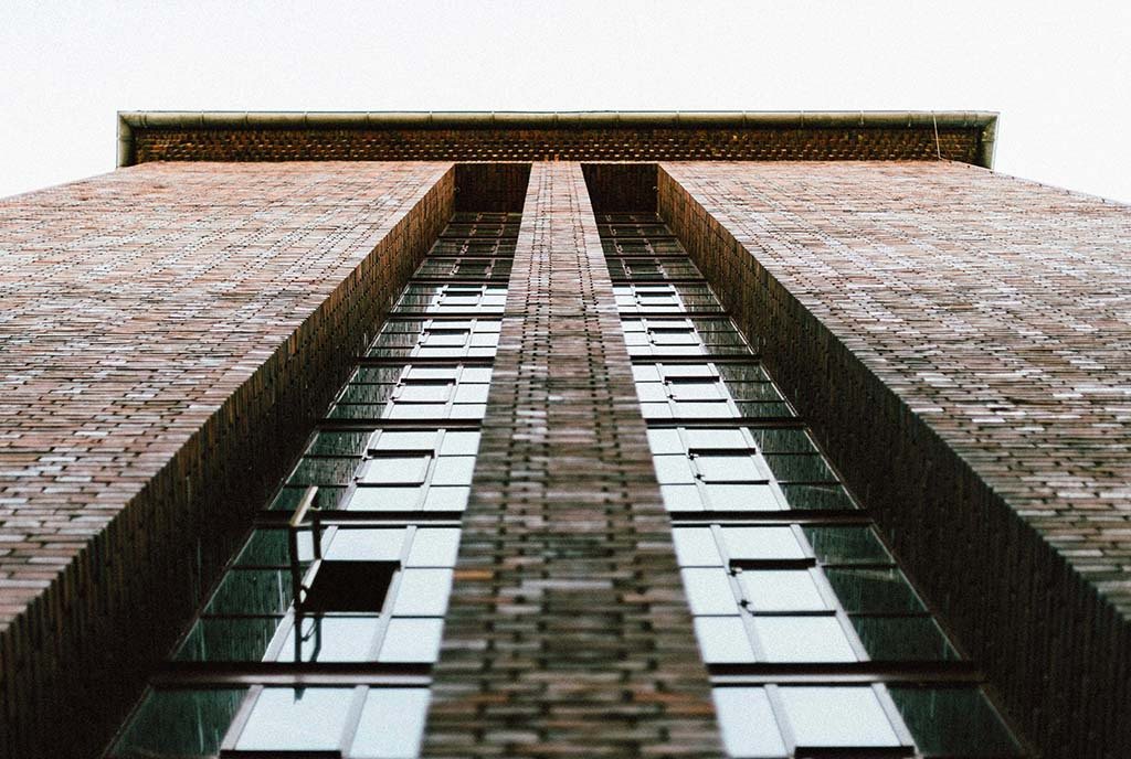 An upward view of a large, brick apartment building. One of the windows of the building is open.