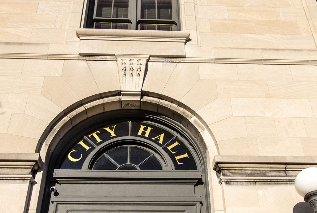 Exterior of a municipal City Hall with the “city hall” sign in the window