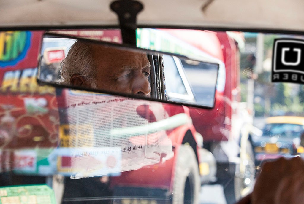 A ride share cab driver lost in his thoughts during Mumbai traffic. Mumbia India. An uber sticker is affixed to the windshield.