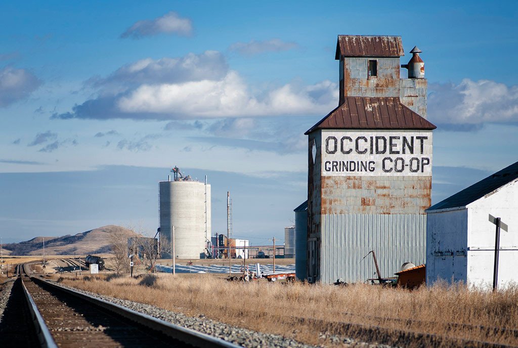 A vintage grain elevator in western North Dakota, reading “Occident Grinding Co-Op” with a modern grain elevator in the background.