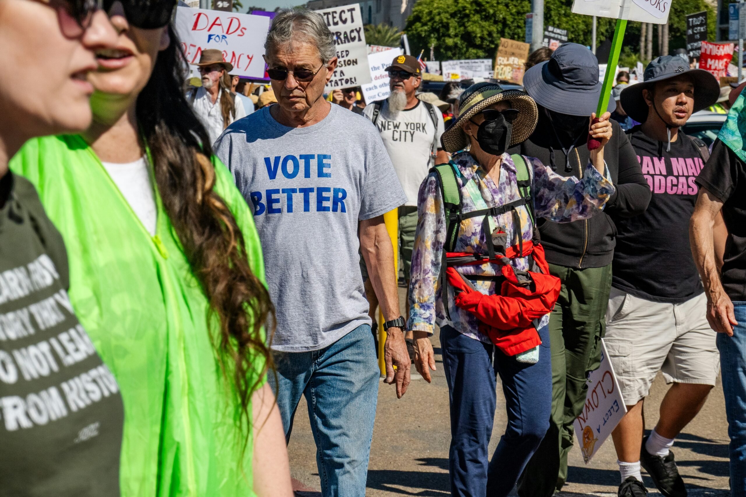 Crowd gathers, with a man in the center wearing a gray "Vote Better" t-shirt.