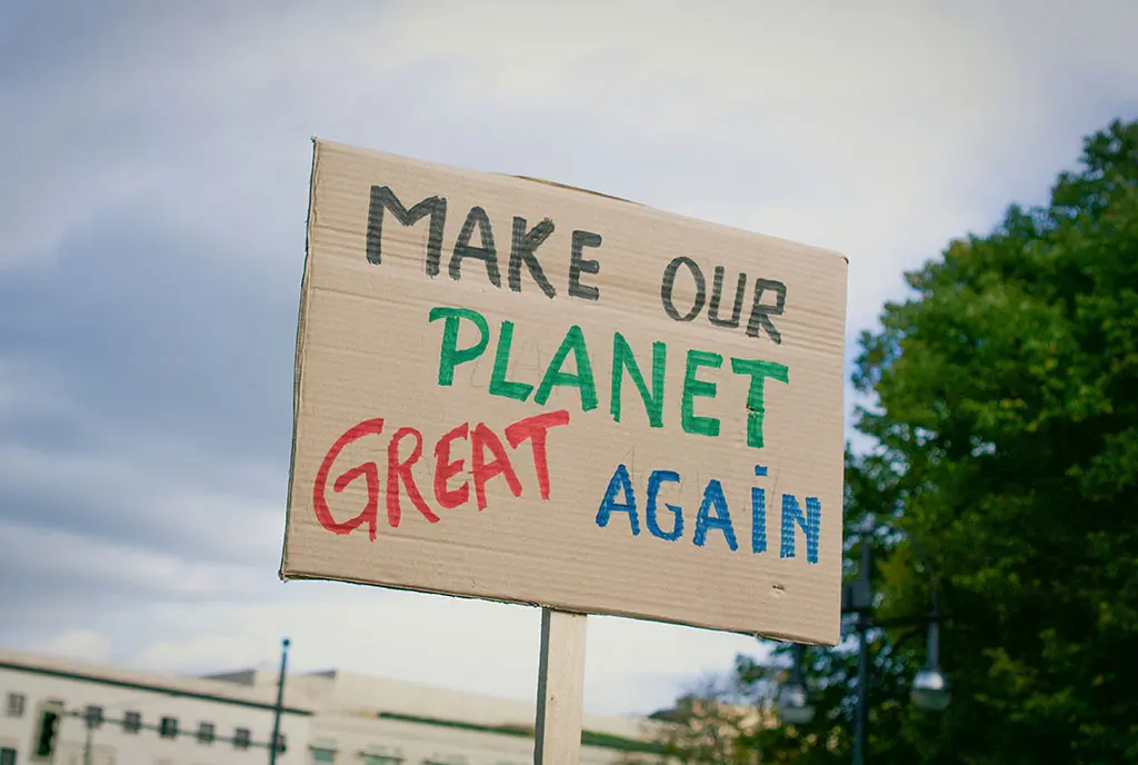 A person holding up a cardboard sign at a local protest that reads, “Make Our Planet Great Again”, which is a play on Trump’s MAGA campaign slogan.