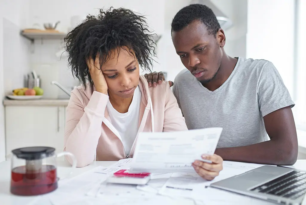 A young Black couple grappling with bills together, representing rising poverty and the inability of families to meet financial needs.