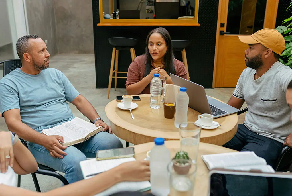 A group of diverse leaders in a roundtable discussion, representing the dual focus on local communities and systemic change.