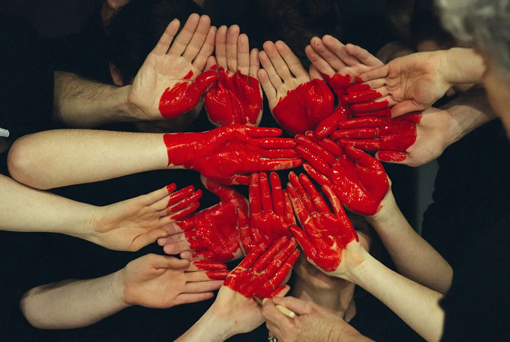 A red heart, formed by a group of people with painted hand palms, symbolizing solidarity in giving among the many.