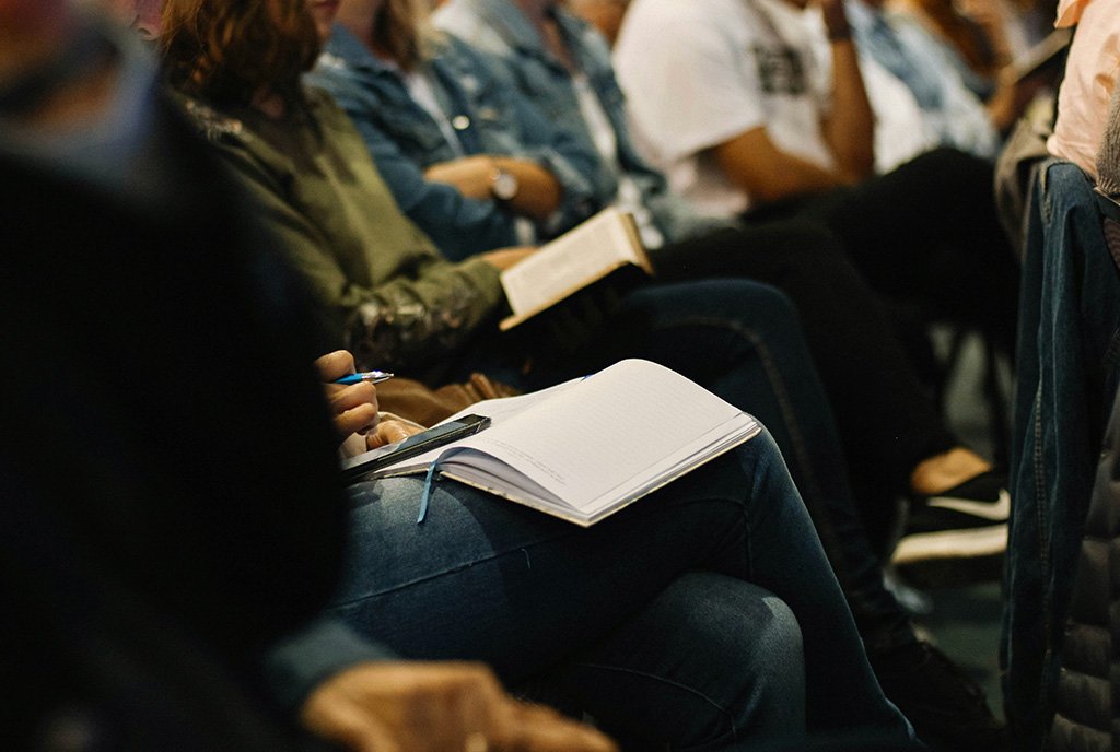 A diverse group of individuals in a town hall meeting, listening, taking notes, and engaging as passionate community members.