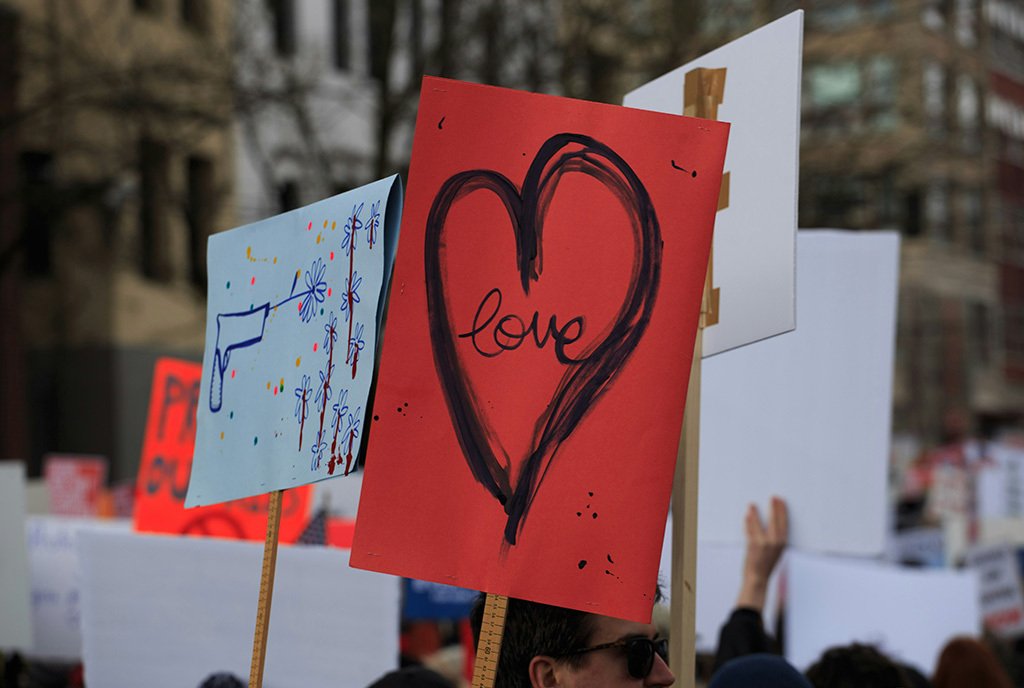 A person holds up a red protest sign depicting the simple word “Love” surrounded by a heart at March for Our Lives in Seattle.