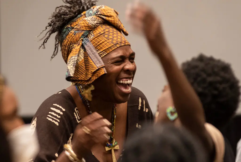 Facing Race participants, including a Black woman with a kente cloth headscarf tied around her head, dance and move in joy.