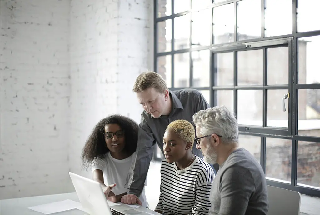 A dvierse group of workers gathered around a computer screen and looking at data together, symbolizing AI integration in the sector.