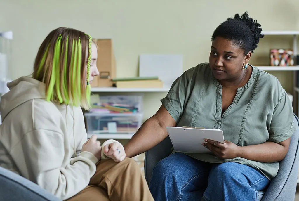 A social worker talking empathetically with a young patient donning green highlights, representing personalized care and the humanity offered by cooperative models.