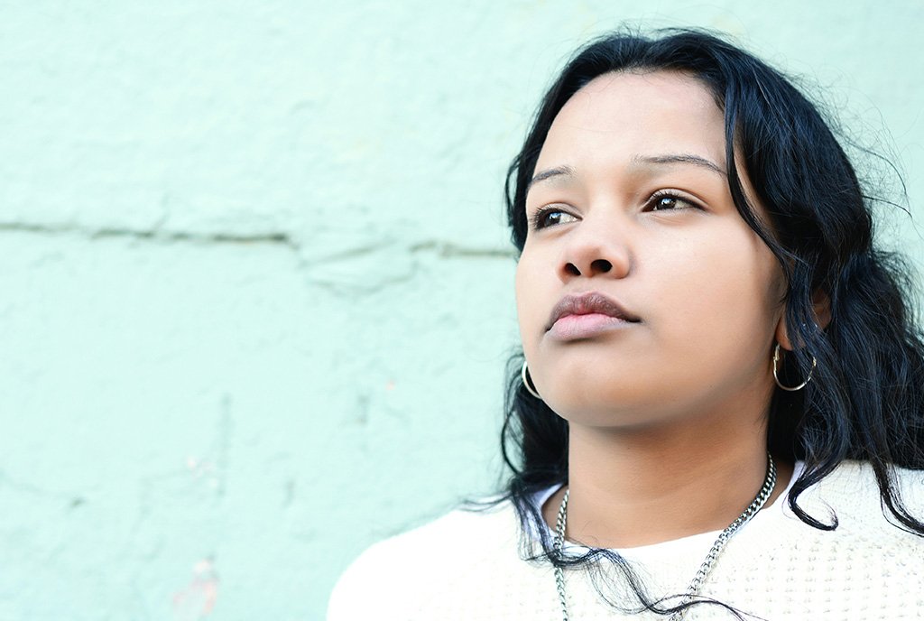 A young South American woman stares into the distance with a serious look on her face, as if contemplating her future.