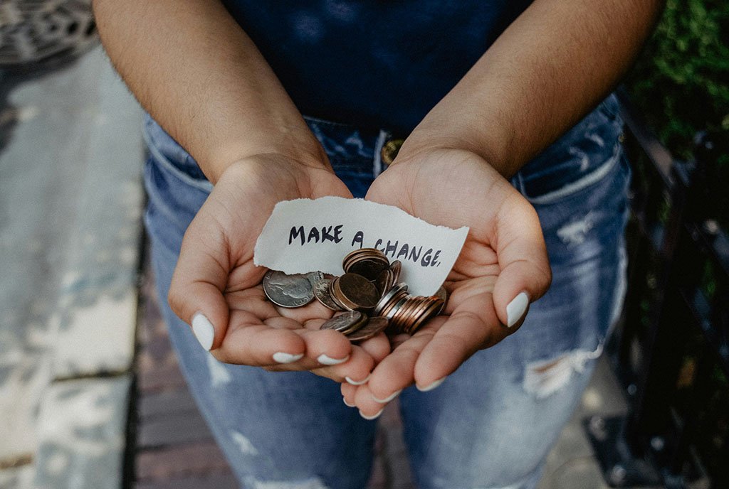 A person holding a palm-full of change with a hand-written note that reads, “Make A Change”, symbolizing the power that people have to muster grassroot financial support for organizations that have personally impacted them.