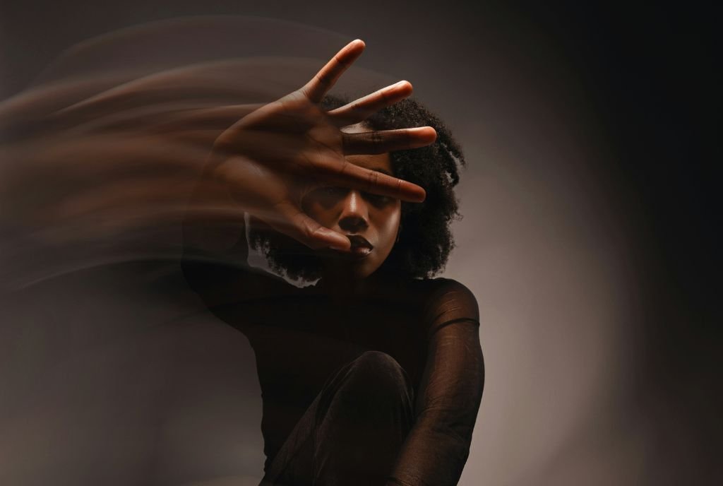 A long exposure of a young Black woman moving her hand to obscure her face, symbolizing the erasure of diverse communities from the language of many nonprofits.