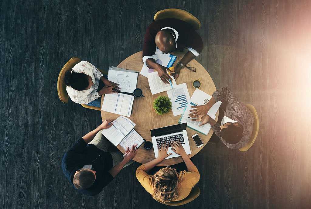 A circular table where a diverse board is brainstorming with visual aids like sticky notes and flowcharts, emphasizing inclusion and interdependence.