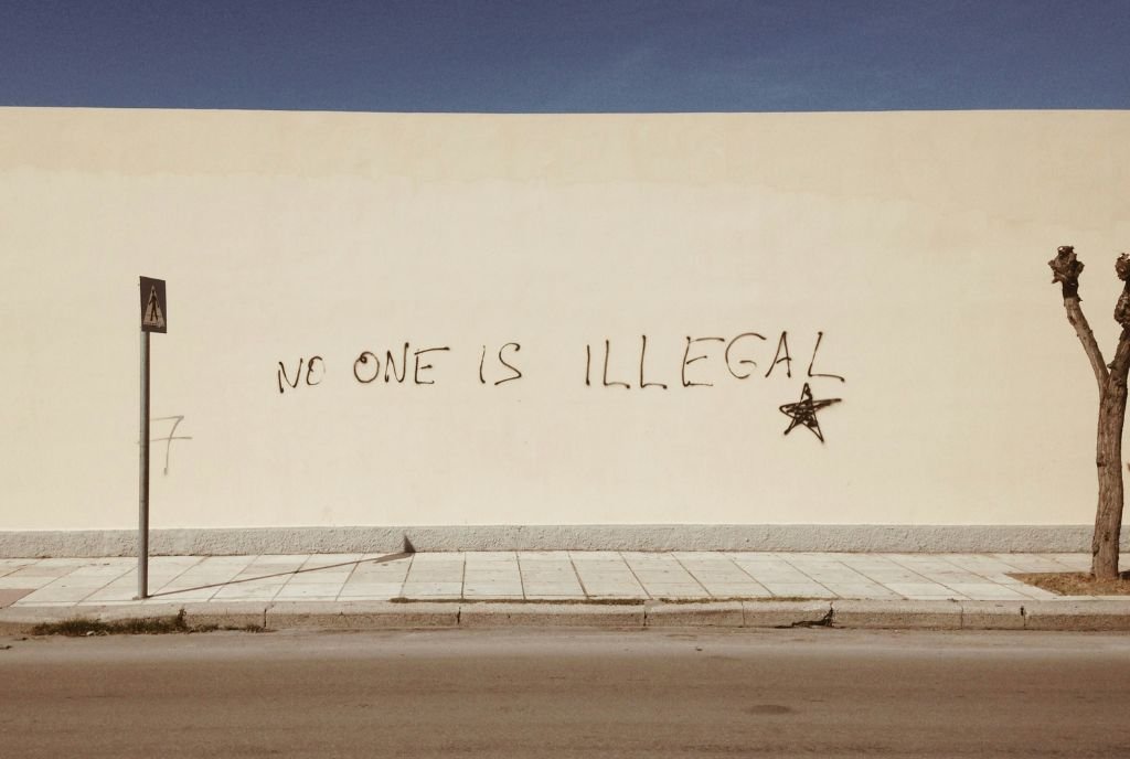 Writing on a wall that reads, “ No one is illegal.”