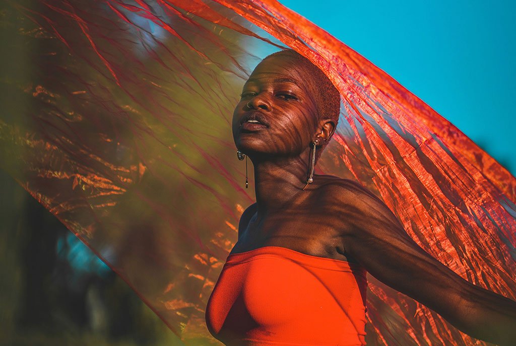 A Black woman waving an iridescent orange fabric over her head while dancing in a field, illustrating the theme of reclamation and self-determination.