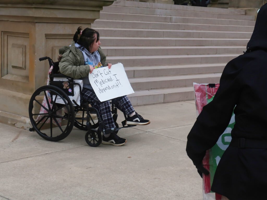 "A young woman in a wheelchair holds a handmade sign that reads, 'Don't Cut Medicaid. I depend on it!!!'