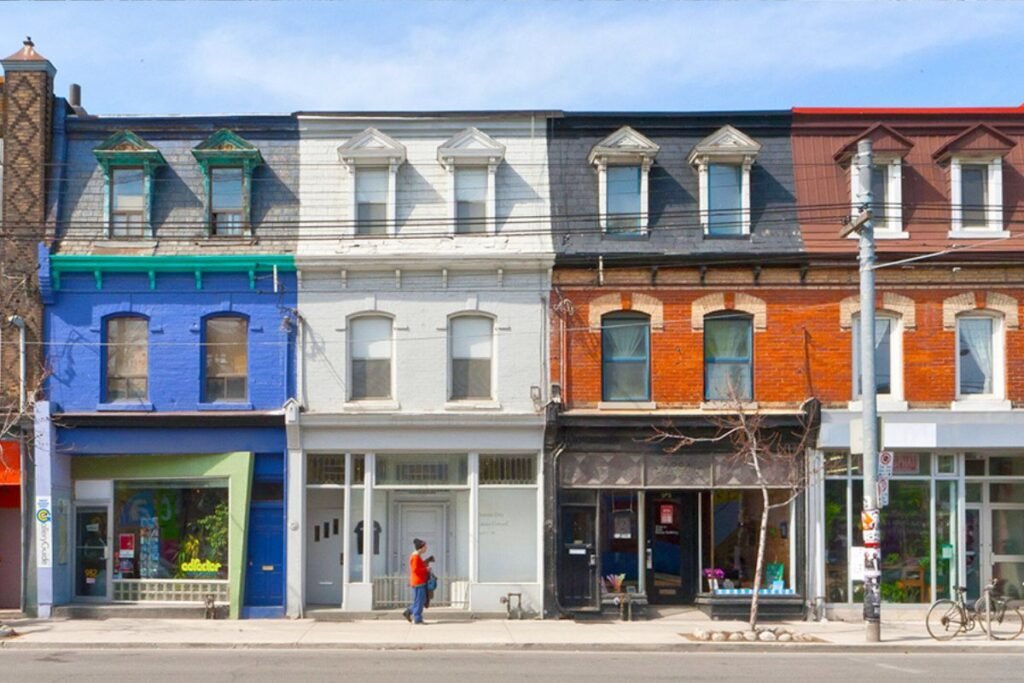 A set of row houses painted in different colors with first floor retail and two stories of residences above on a small-town business main street.