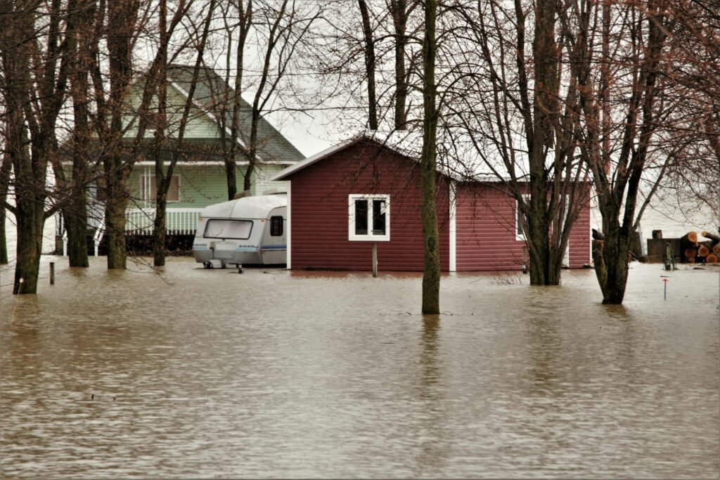 A green and red house and an RV are pictured among the trees, surrounded by multiple feet of floodwater.