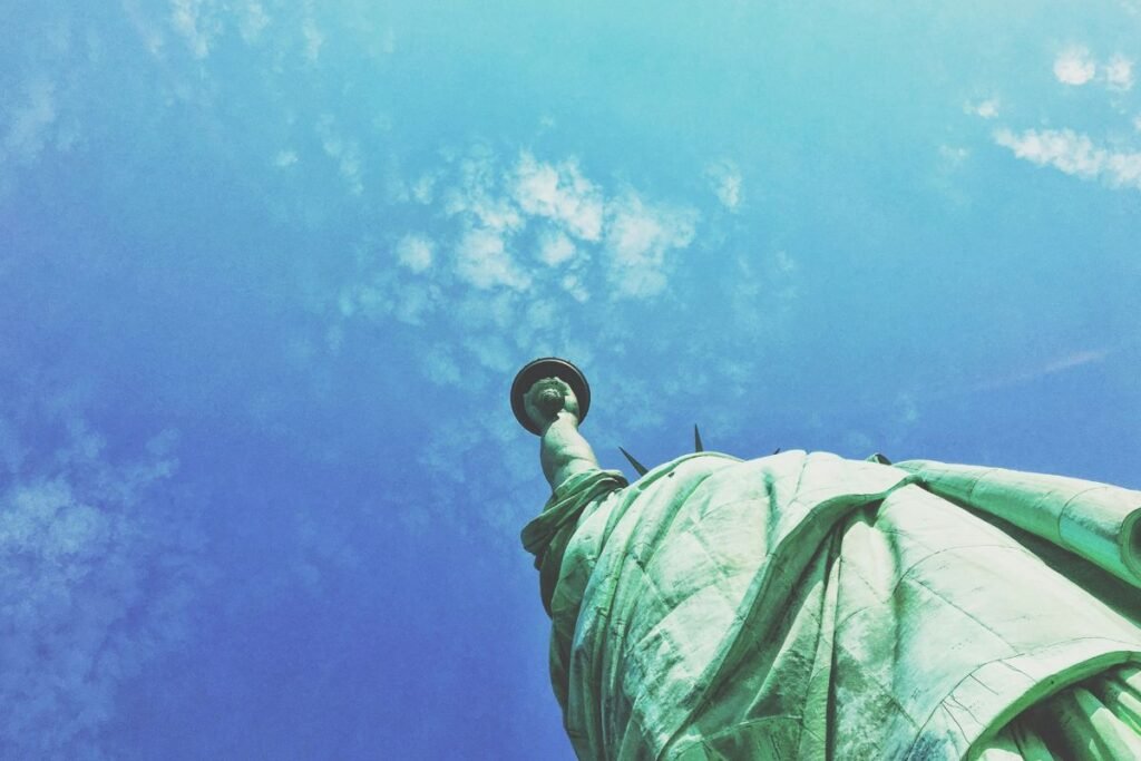 The Statue of Liberty, seen from below, with the torch rising into a blue sky with white clouds.