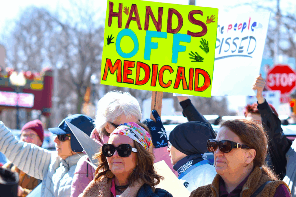 A crowd attending a rally in support of Medicaid. One person holds a prominent sign that reads "Hands Off Medicaid".
